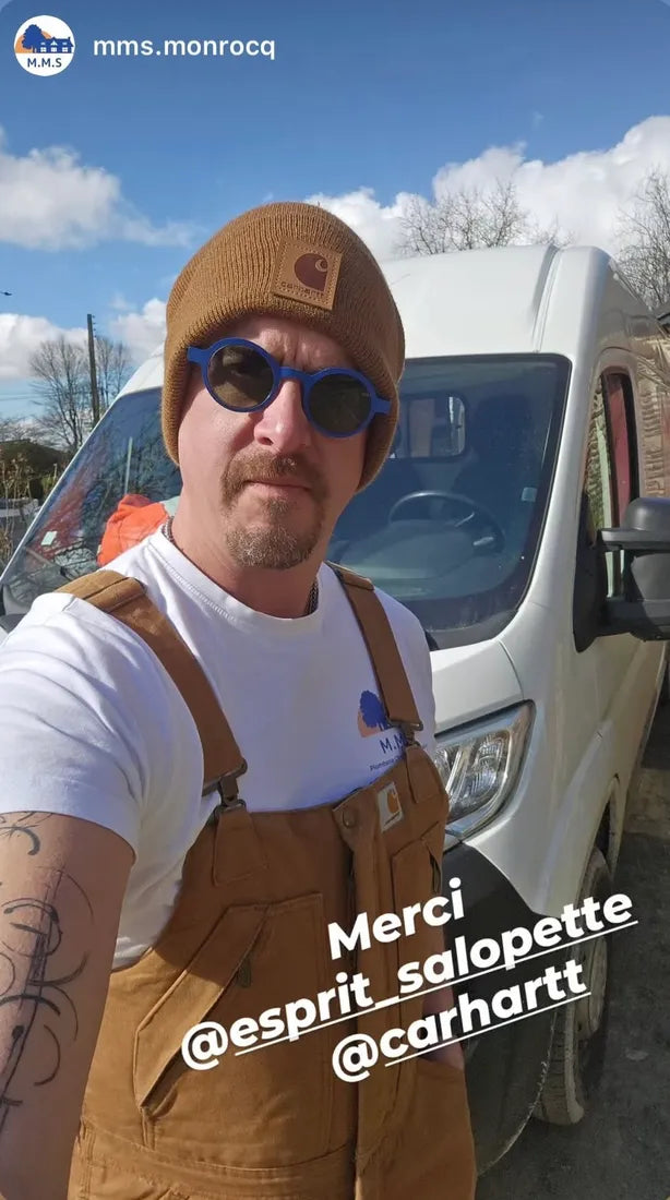 David en salopette Carhartt marron, bonnet Carhartt et lunettes bleues, devant un utilitaire