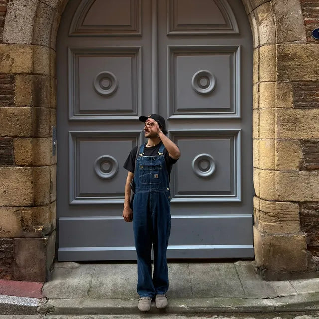 Homme en salopette Carhartt Denim portée longue, t-shirt noir et casquette, en ville