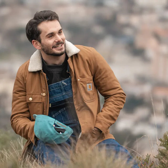 Homme en salopette Carhartt Denim et veste en toile marron, assis en extérieur